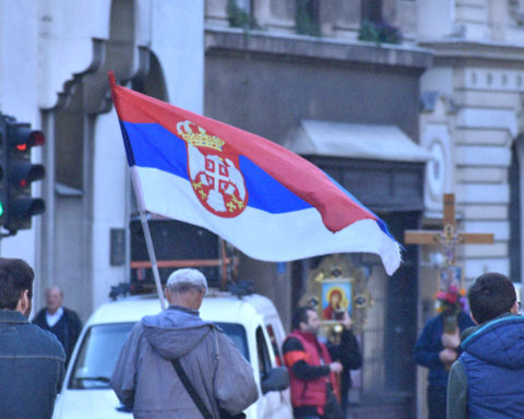 Hombre marcha con bandera serbia en manifestación religiosa