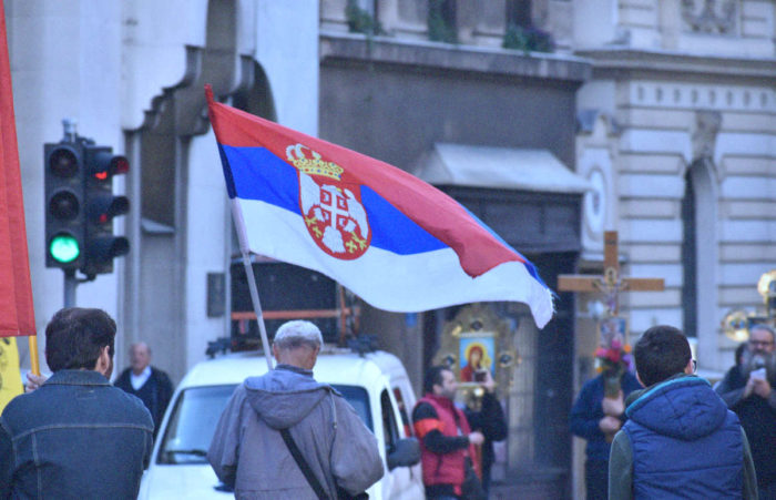 Hombre marcha con bandera serbia en manifestación religiosa