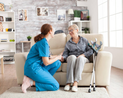 Anciana feliz en una residencia sentada en un sofá hablando con su cuidador. Mujer jubilada con muletas