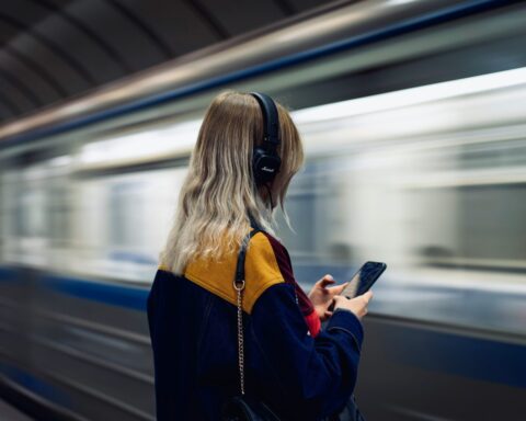 Mujer de espaldas escuchando música con audífonos mientras espera el metro