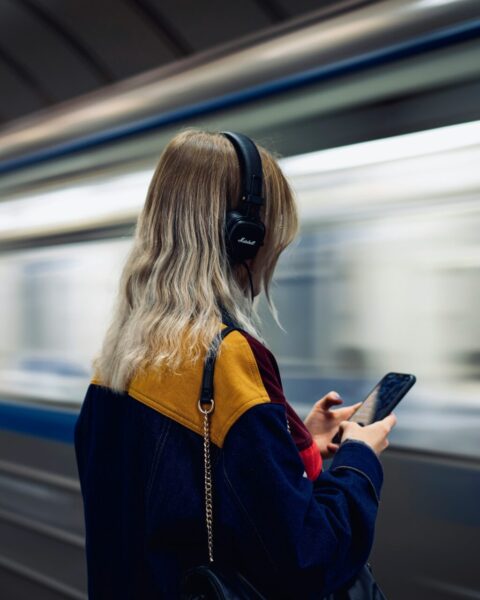 Mujer de espaldas escuchando música con audífonos mientras espera el metro
