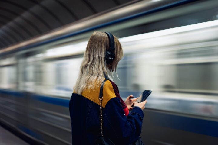 Mujer de espaldas escuchando música con audífonos mientras espera el metro