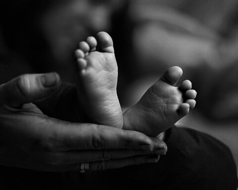 Imagen en primer plano de unos diminutos pies de bebé recién nacido, sostenidos entre las manos protectoras de uno de los padres