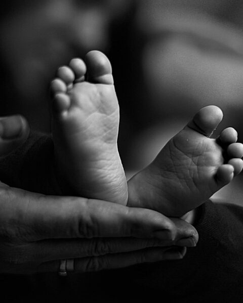 Imagen en primer plano de unos diminutos pies de bebé recién nacido, sostenidos entre las manos protectoras de uno de los padres