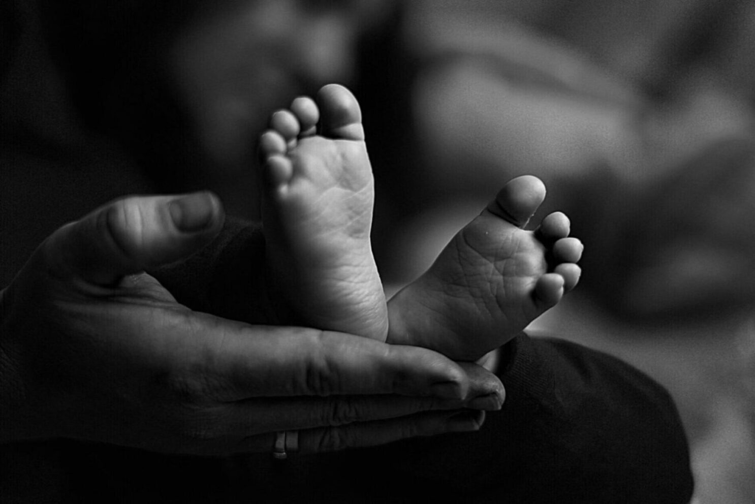 Imagen en primer plano de unos diminutos pies de bebé recién nacido, sostenidos entre las manos protectoras de uno de los padres