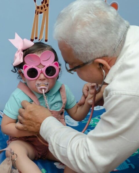 Médico examinando a una niña con estetoscopio en una consulta de pediatría y masculinidades.